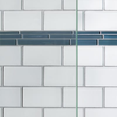 White subway tiles with a single vertical stripe of blue accent tiles and glass shower doors.
